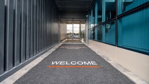 Una entrada de hotel moderna con alfombra oscura, barandales de metal y puertas de vidrio.