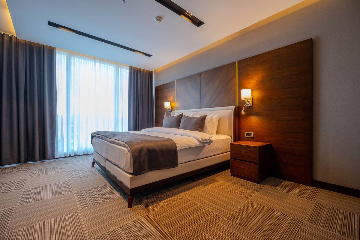 A modern hotel room with a large bed, a nightstand, and a wall-mounted lamp.