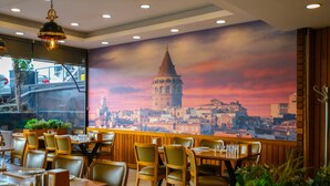 Un restaurante con mesas y sillas de madera, un mural con un paisaje urbano en la pared y vistas de la ciudad a través de grandes ventanales.
