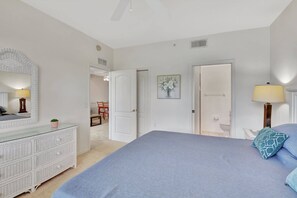 Quarto com uma cama grande, cômoda, espelho e porta de acesso a um banheiro.