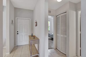 Un couloir avec une porte blanche, une petite table sur laquelle se trouvent un vase et une bougie, et un placard aux portes à persiennes.