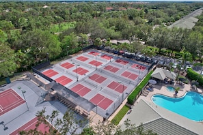 Vue aérienne d’un complexe sportif comprenant plusieurs courts de tennis, une piscine et des espaces verts environnants.