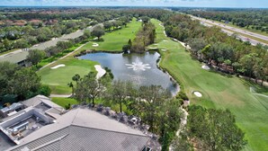 A golf course with a pond, surrounded by trees and a highway. - Cypress Woods for Seasonal or Summer Stays W Golf (Naples)