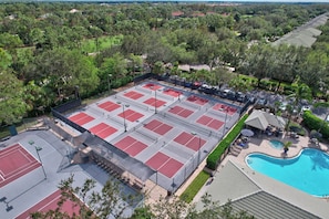 A tennis court complex with multiple courts, a swimming pool, and surrounding greenery.