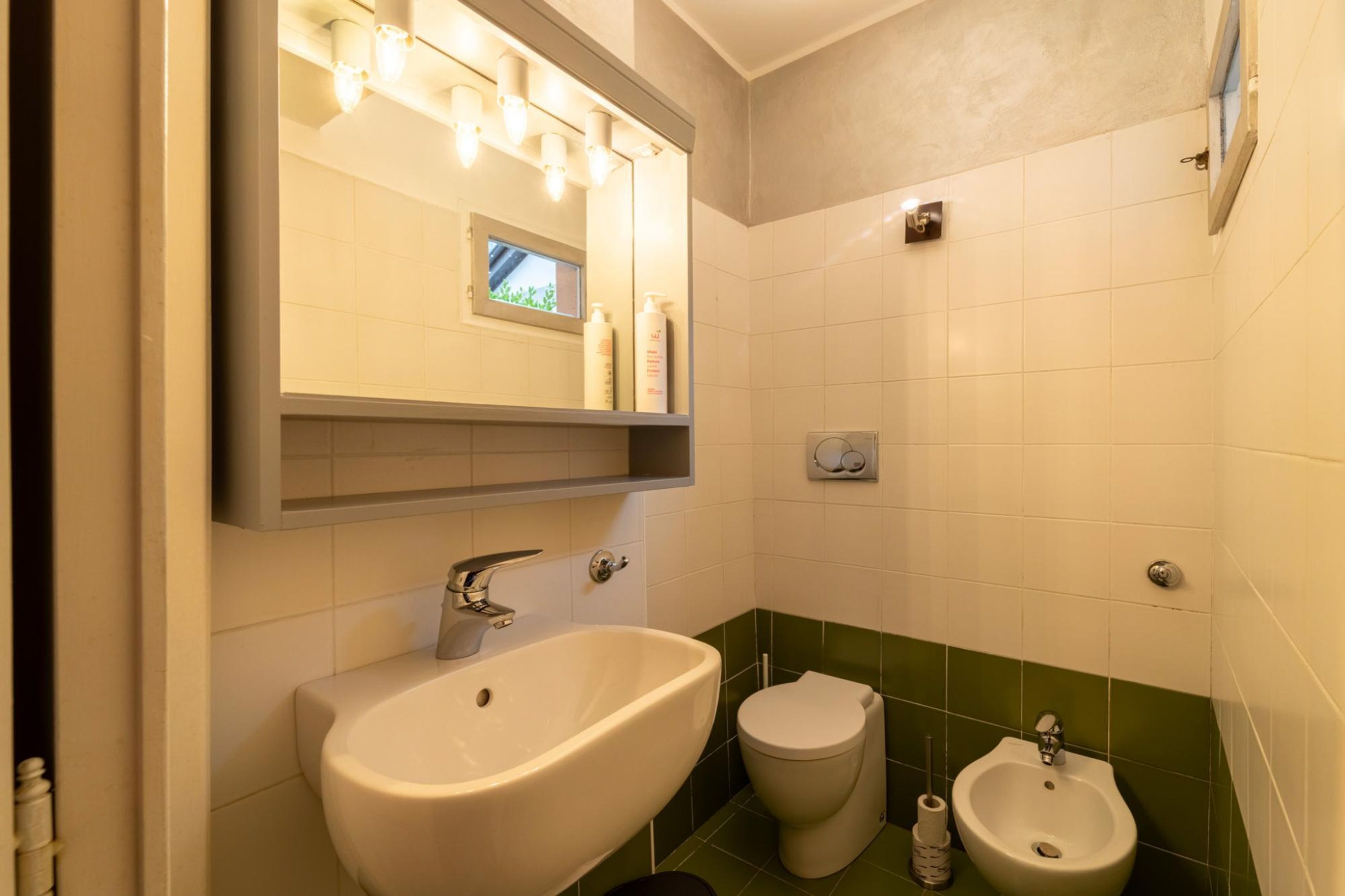 Une salle de bain équipée d’un lavabo, de toilettes, d’un bidet et d’un miroir avec éclairage.