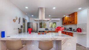 A modern kitchen with a marble island, wooden cabinets, and a central range hood. - Family getaway in this charming townhouse just steps away from Yal Ku Laggon! (Akumal)