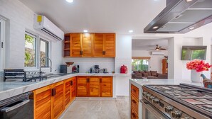 A modern kitchen with wooden cabinets, a gas stove, and a coffee maker. - Family getaway in this charming townhouse just steps away from Yal Ku Laggon! (Akumal)