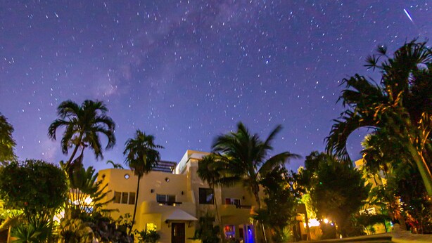 A nighttime scene with a starry sky, a swimming pool, palm trees, and a building with a light-colored facade. - Family getaway in this charming townhouse just steps away from Yal Ku Laggon! (Akumal)