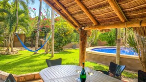 A patio area with a pool, a hammock, and a table with wine glasses. - Family getaway in this charming townhouse just steps away from Yal Ku Laggon! (Akumal)