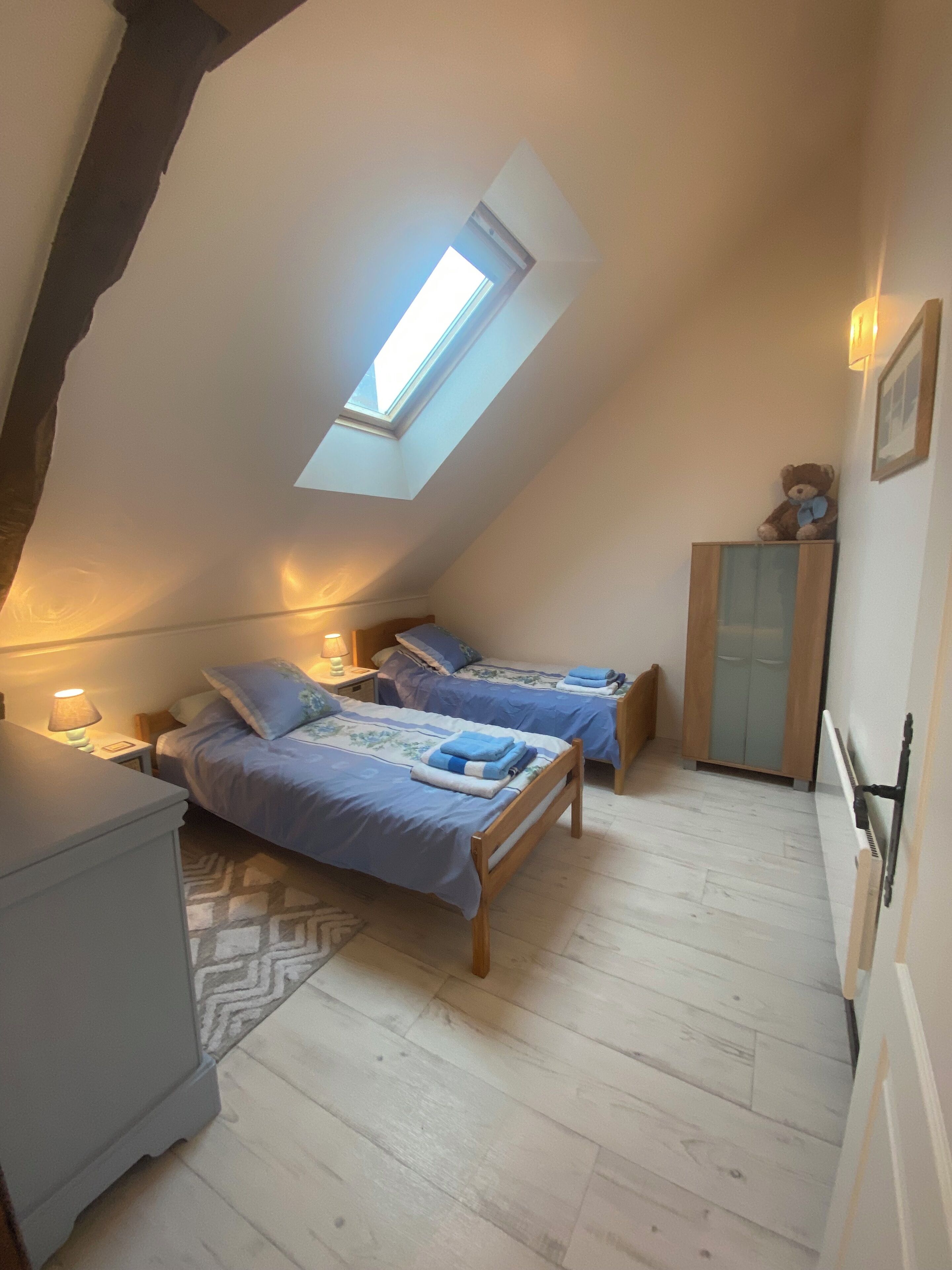 A small, cozy attic bedroom with two beds, a skylight, and a wooden wardrobe.