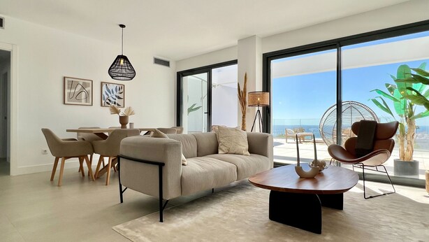 Una sala de estar moderna con un sofá, una mesa de centro y un comedor. Amplias ventanas ofrecen vistas al océano.