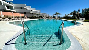 Una piscina azul cristalina con barandillas metálicas, rodeada de sillas de descanso y un edificio moderno al fondo.