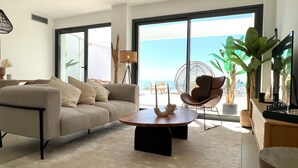 Una sala de estar moderna con un sofá, una mesa de centro y un sillón. Hay un ventanal con vistas al océano.