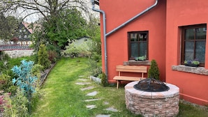 Ein rotes Gebäude mit einem Backstein-Feuerkorb, einer Holzbank und einem kleinen Baum.