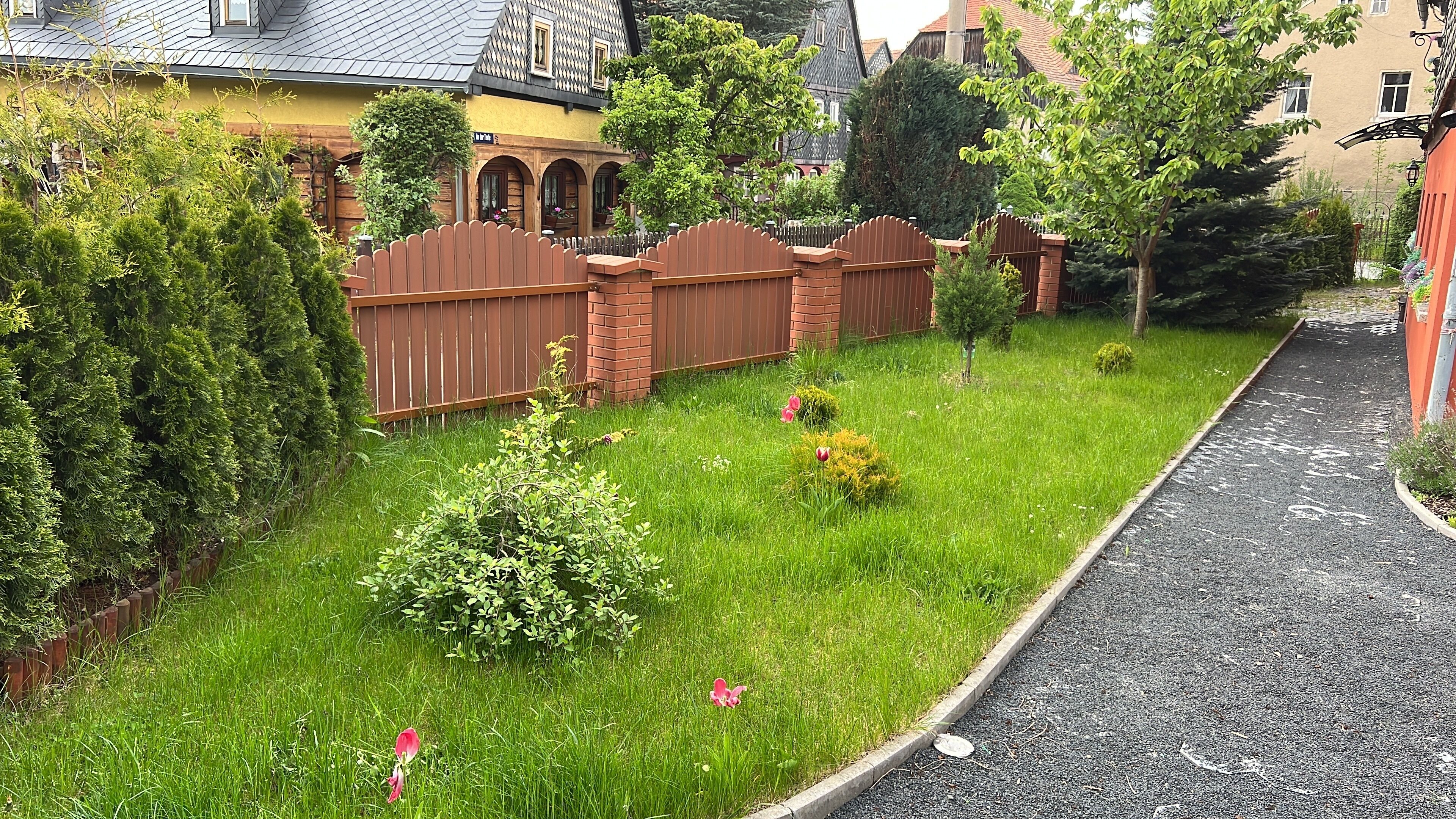 En välskött trädgård med ett trästaket, en grusgång och ett stort utbud av buskar och blommor.