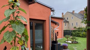 Ein Haus mit gepflastertem Gartenweg, einer großen Pflanze mit gelben Blüten und einem Fenster mit dekorativer Folie.