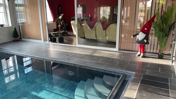 Ein moderner Innenpool mit Glasbarriere, eine Sitzecke mit einer Couch und Sesseln sowie eine Kühlpflanze.