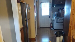 A narrow hallway with wooden flooring, a refrigerator, a freezer, and a microwave. There is a door at the end of the hallway leading to another room. - Private 3-bedroom ranch, 10 miles from Bethany Beach, on a dead-end street. (Dagsboro)