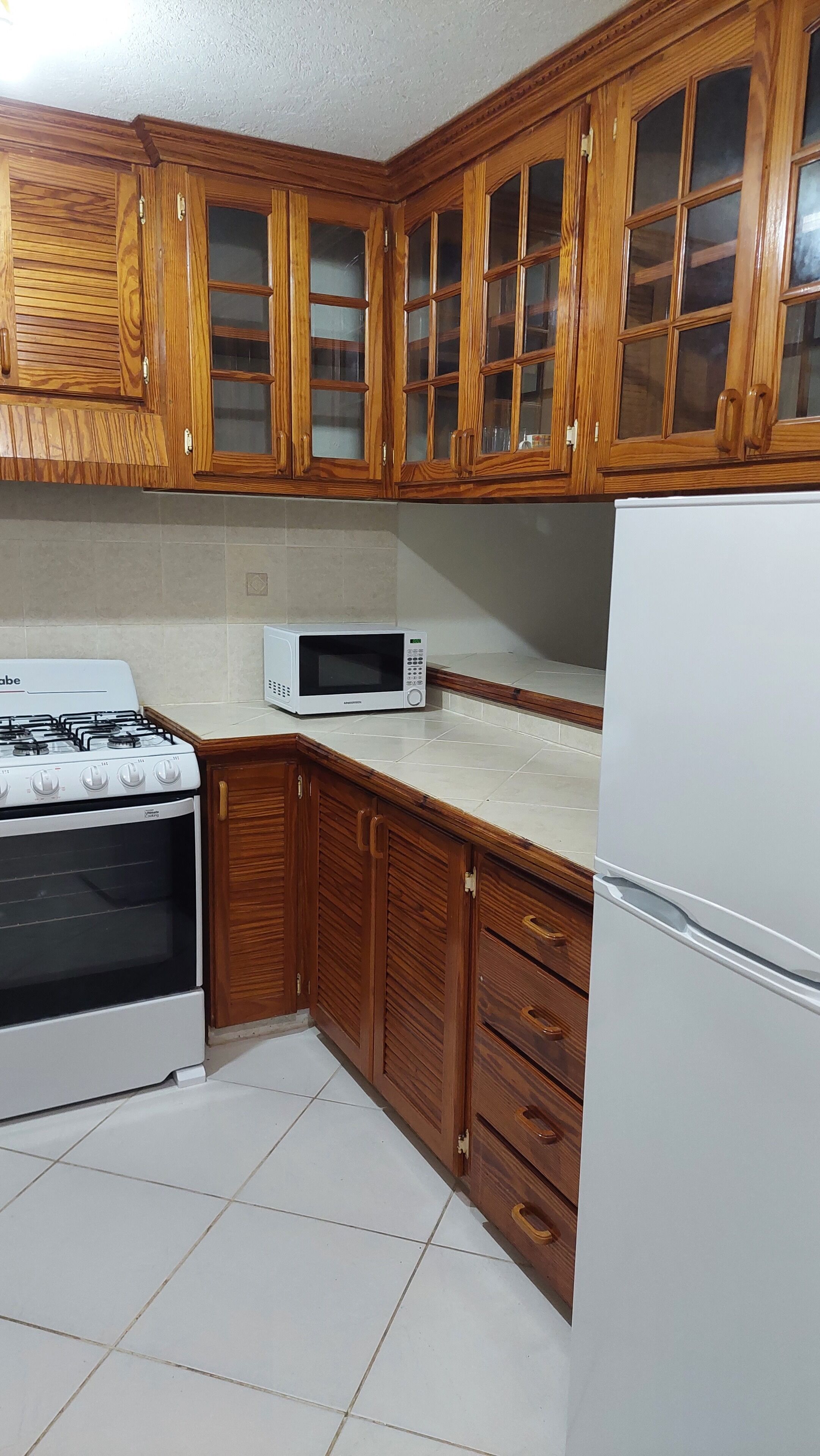 Una cucina con mobili in legno, piano cottura a gas, forno a microonde e frigorifero.