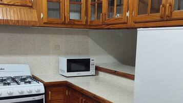 A kitchen with wooden cabinets, a gas stove, a microwave, and a refrigerator.