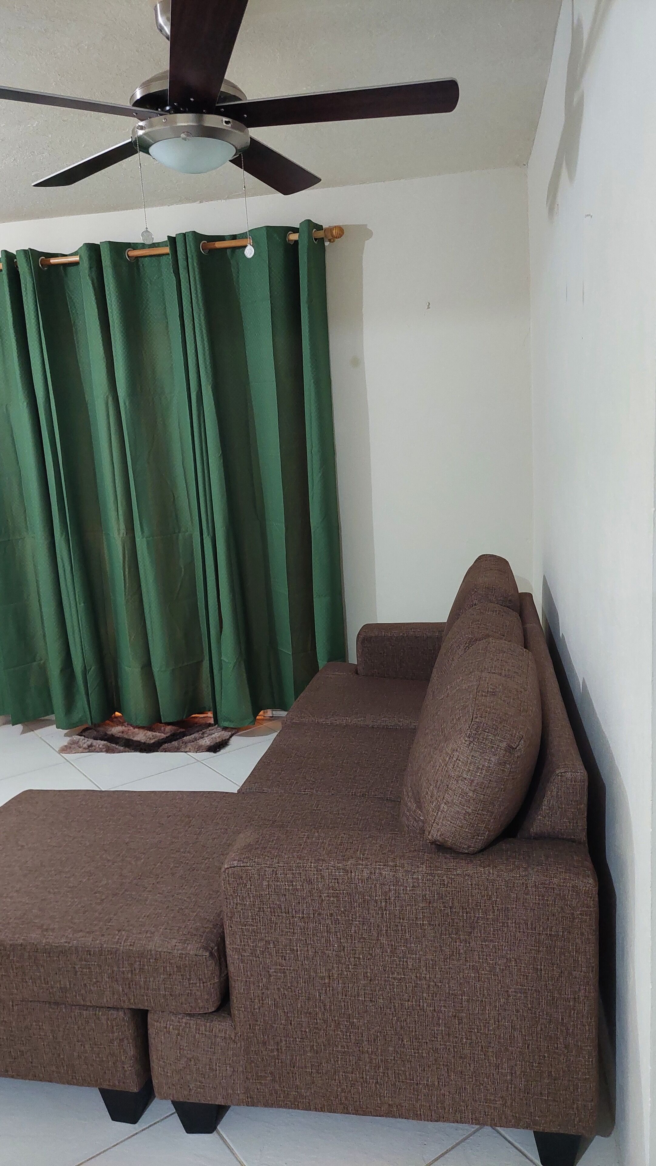 A living room with a brown sofa, a ceiling fan, and green curtains.