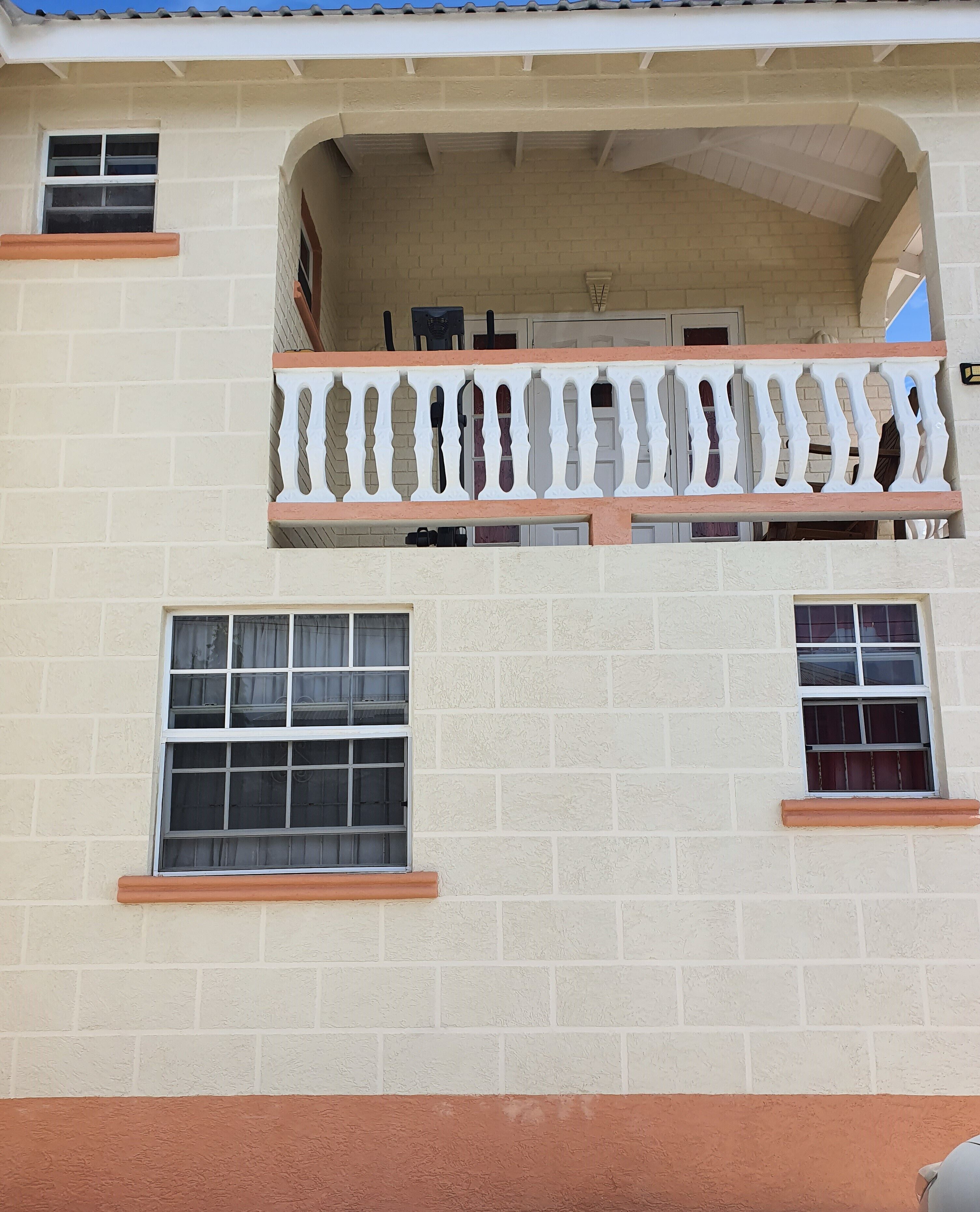 A two-story building with a balcony on the upper floor, featuring a white balustrade and a window with a grid pattern.