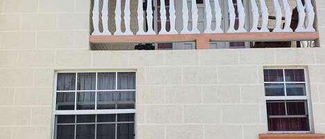 A two-story building with a balcony on the upper floor, featuring a white balustrade and a window with a grid pattern.