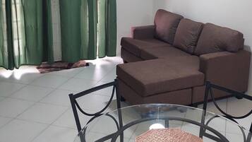 A living room with a brown sofa, a glass coffee table, and a ceiling fan.