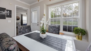 A dining area with a white table, black placemats, and a vase with white flowers. There are two chairs with patterned upholstery and a potted plant on the windowsill. - Beautiful home in great location close to downtown, Nashville Heights (Nashville)