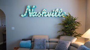 A living room with a light blue couch, a neon sign reading "Nashville," and a potted plant. - Beautiful home in great location close to downtown, Nashville Heights (Nashville)