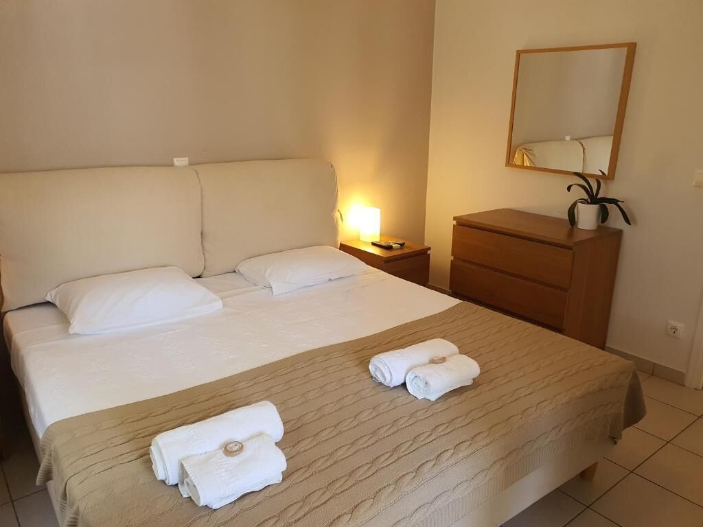 Una camera d'albergo con un letto grande, un comodino con una lampada, una cassettiera in legno e uno specchio a parete.