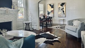 Una sala moderna con chimenea, una mesa redonda de centro, un sofá y un comedor con mesa y sillas. Hay cuadros abstractos en la pared y una alfombra con estampado de cebra en el suelo.