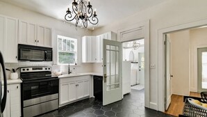 Una cocina moderna con armarios blancos, un microondas negro, electrodomésticos de acero inoxidable y un piso de baldosas hexagonales.