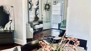 Un comedor con mesa de madera, sillas y un jarrón de flores. Hay un cuadro en la pared y una puerta decorada con un adorno navideño.