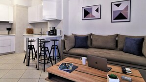 A modern living space with a kitchen, a sofa, a coffee table, and a laptop. - IQ Kleovoulou (Athens)