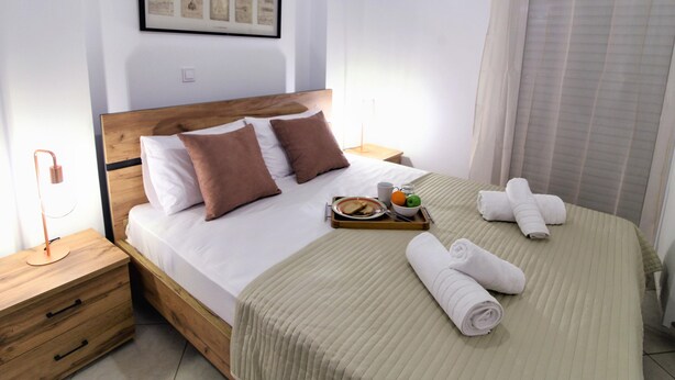 A neatly made bed with pillows, a tray with breakfast items, and rolled towels. - IQ Kleovoulou (Athens)