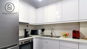 A modern kitchen with white cabinets, a stainless steel refrigerator, a microwave, a coffee maker, and a red appliance on the counter. - IQ Kleovoulou (Athens)