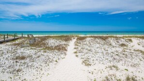 A beach with a wooden boardwalk leading to the water, sandy dunes, and a clear blue sky.