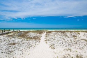 A beach with a wooden boardwalk leading to the water, sandy dunes, and a clear blue sky.
