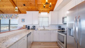 A modern kitchen with white cabinets, stainless steel appliances, and a wooden ceiling.