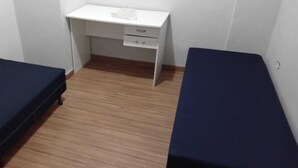 Pieni huone, jossa on kaksi erillistä sänkyä, työpöytä tuolilla ja puulattia.