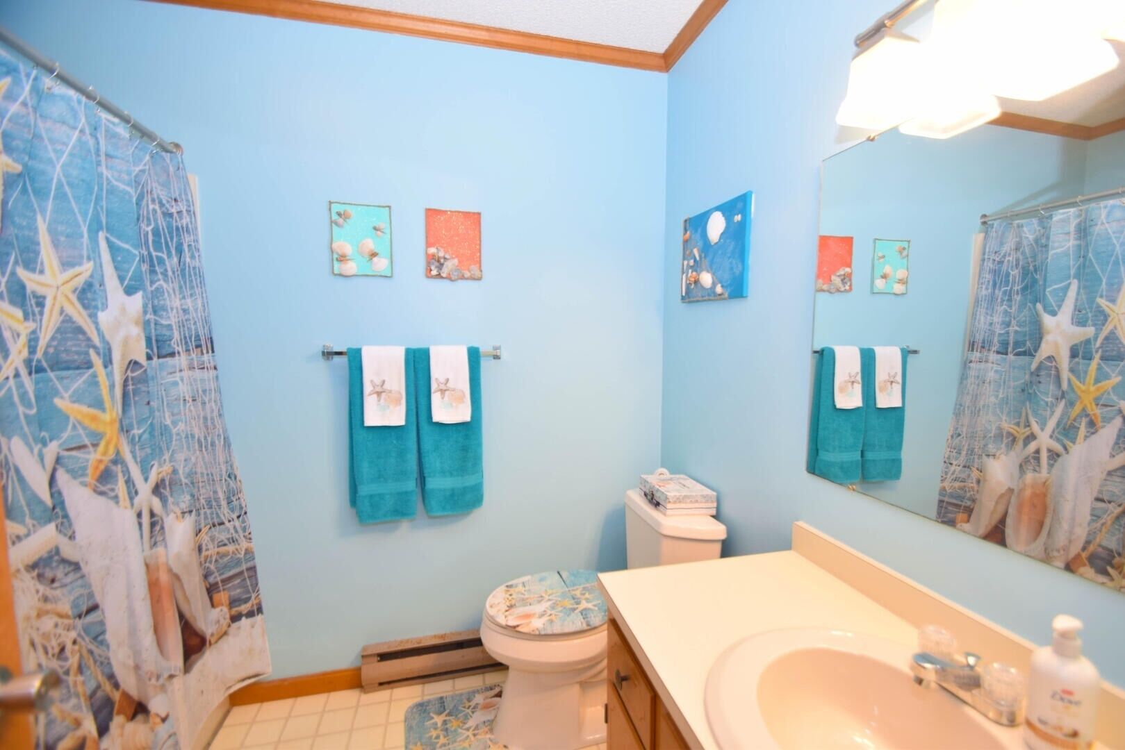 Une salle de bain avec un mur bleu, des toilettes blanches, un lavabo avec un miroir et des décorations sur le thème des étoiles de mer.