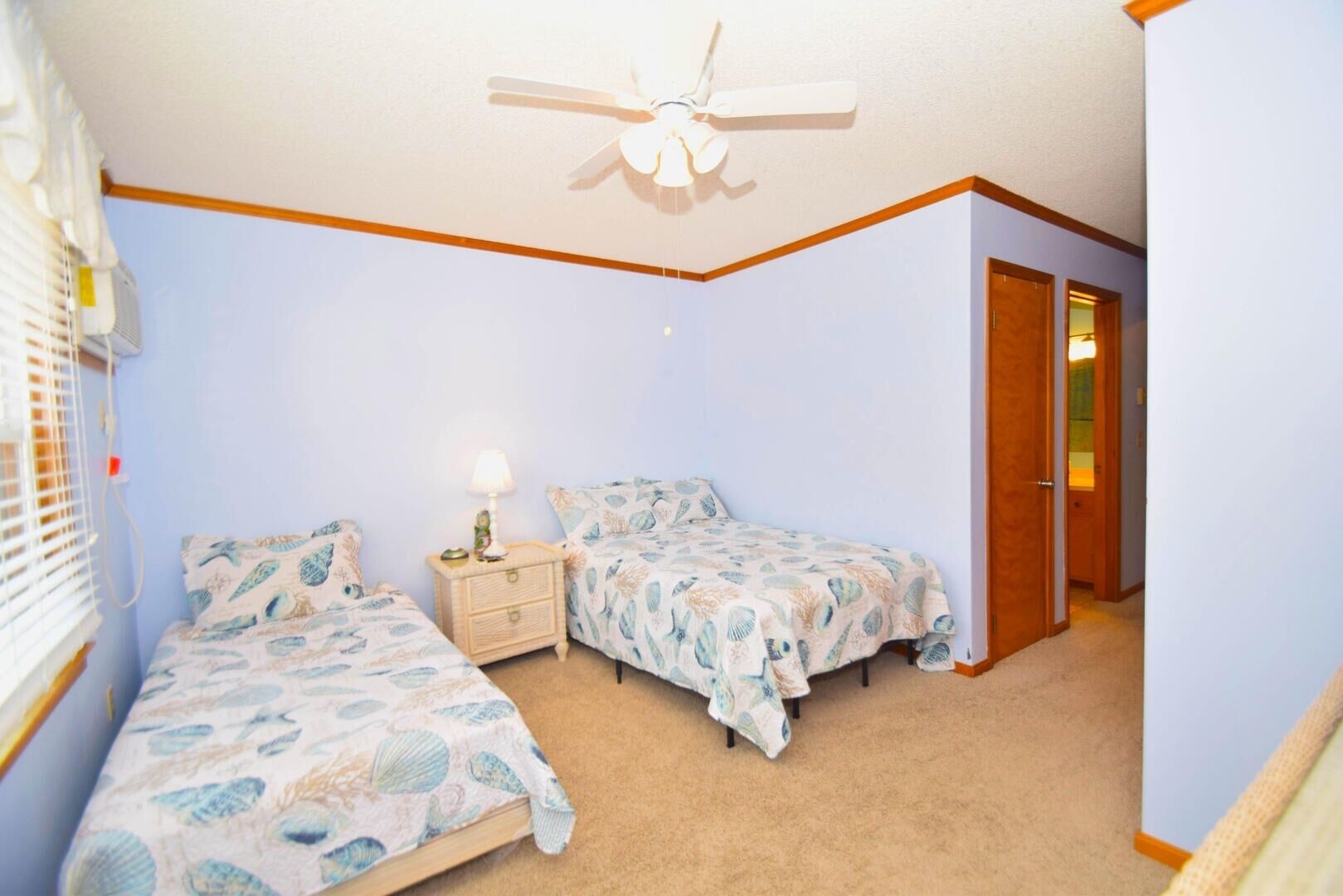 Une chambre avec deux lits, un ventilateur de plafond et une table de chevet avec une lampe.
