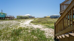 Ein Sandstrandabschnitt mit mehreren Strandhäusern und einer Holzterrasse.
