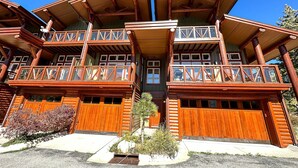 Una cabaña de troncos de varios pisos con balcones, puertas de garaje de madera y cielo despejado.