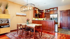 A modern kitchen with wooden cabinets, a stainless steel refrigerator, and a dining area with a rug and chairs. - Juniper Crest #2 3 Bedroom Townhouse by RedAwning (Mammoth Lakes)