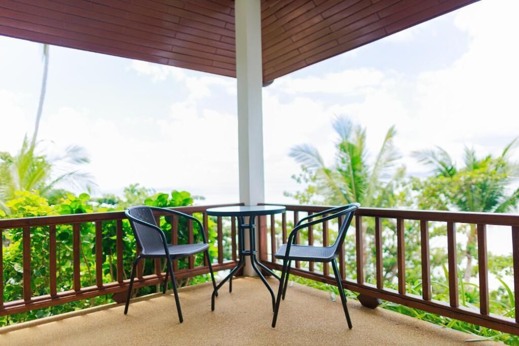 A covered outdoor seating area with two tables and chairs, surrounded by a wooden railing, overlooking a lush green landscape.