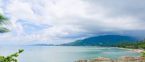 A coastal landscape with clear water, rocky formations, and distant mountains.