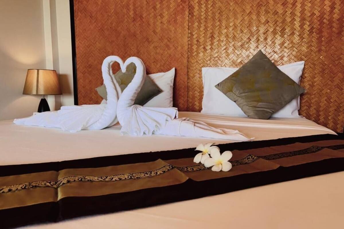 Uma cama bem arrumada com arranjo de toalhas em formato de coração, um travesseiro decorativo e uma flor sobre o lençol.