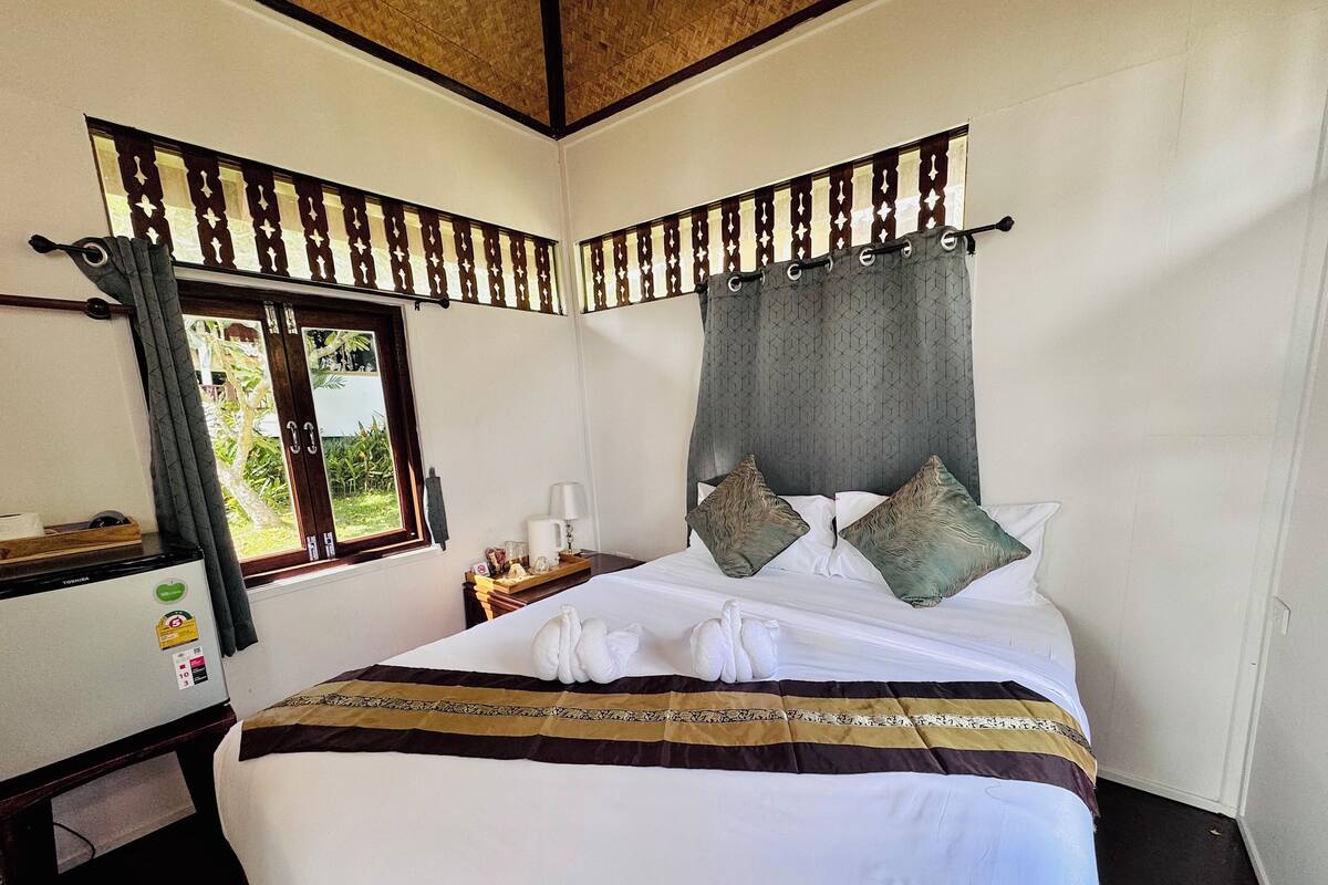 Quarto de hotel com cama, escrivaninha, frigorífico e janela com cortinas.